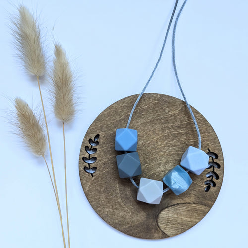 A photo of a baby teething necklace with five blue beads on a wooden disc background