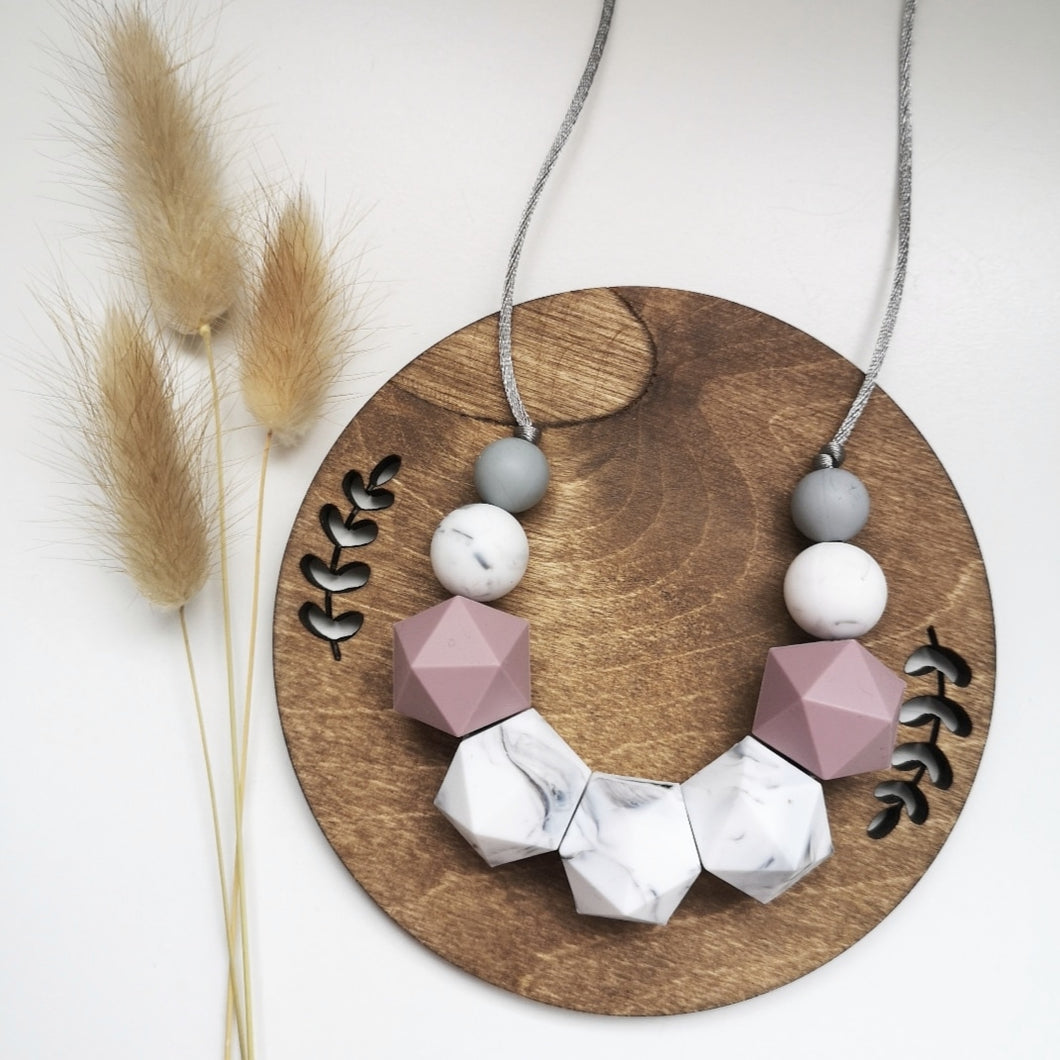 A silicone teething and breastfeeding fiddle necklace in contrasting marble, mauve and grey beads on a soft grey cord with varying textures.